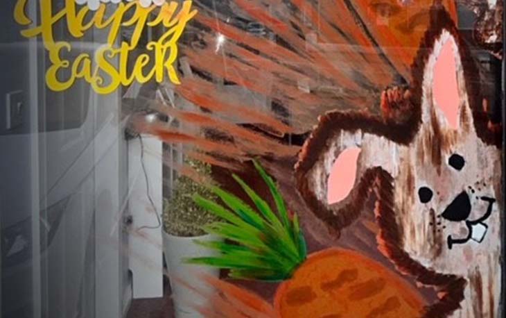 Picture of a window display with a hand painted Easter bunny holding a carrot, with Happy Easter in the top left.